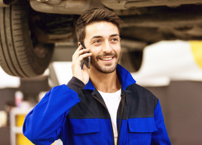service technician standing in auto service bay talking to customer